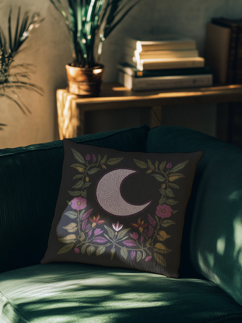 Black woven throw pillow with an embroidered crescent moon and floral pattern in soft ivory, green, purple, and gold, featuring a textured finish.
